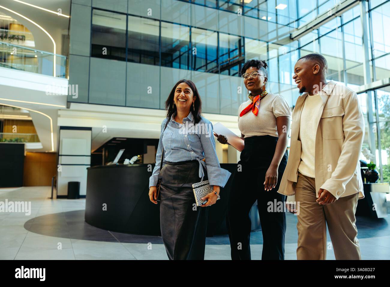 Trois collègues s'engagent dans la conversation tout en se promenant dans un hall d'entrée contemporain d'espace de bureau, mettant en évidence le travail d'équipe et la croissance professionnelle de l'entreprise Banque D'Images