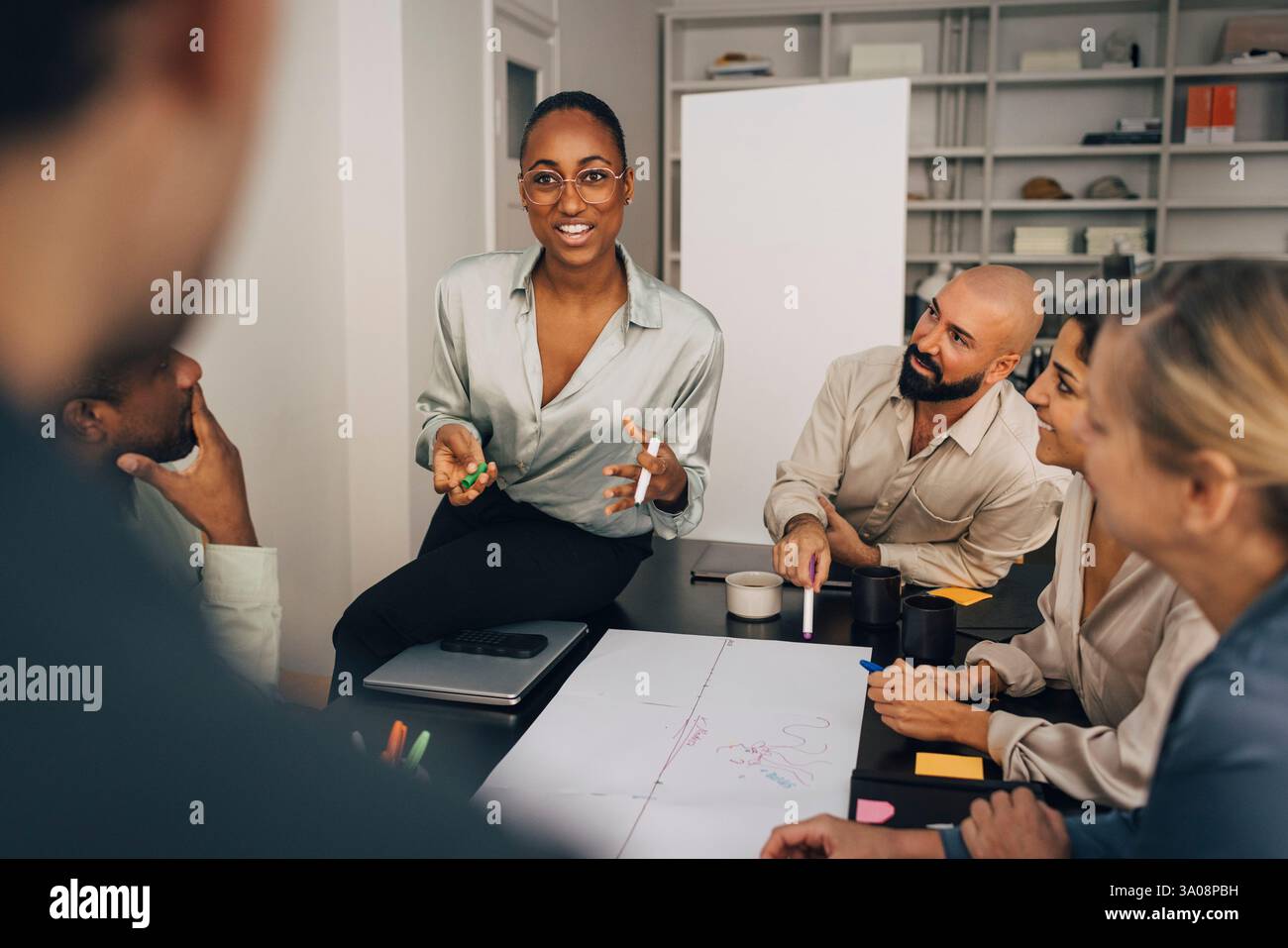 Femme d'affaires souriante discutant du plan d'affaires avec des collègues masculins et féminins lors de la réunion au bureau créatif Banque D'Images