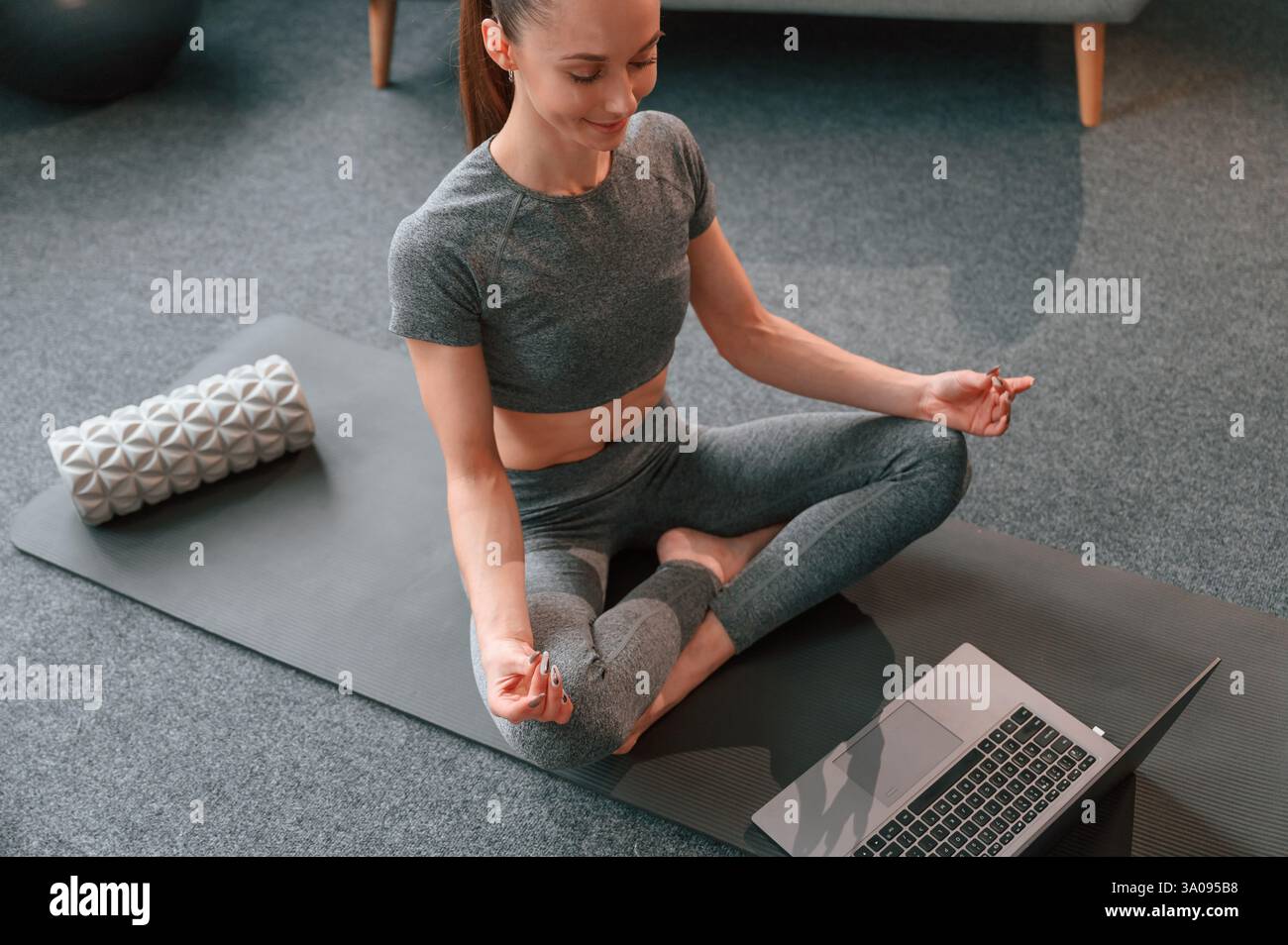 Prendre des leçons en ligne en utilisant un ordinateur portable. Jeune femme dans des vêtements de yoga faisant du fitness à l'intérieur. Banque D'Images