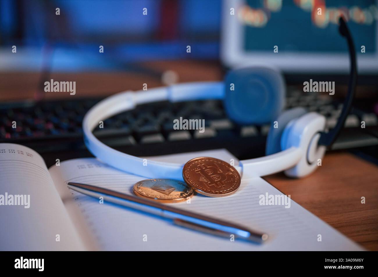 Vue rapprochée des bitcoins physiques, écouteurs, bloc-notes et stylo qui est sur la table. Banque D'Images