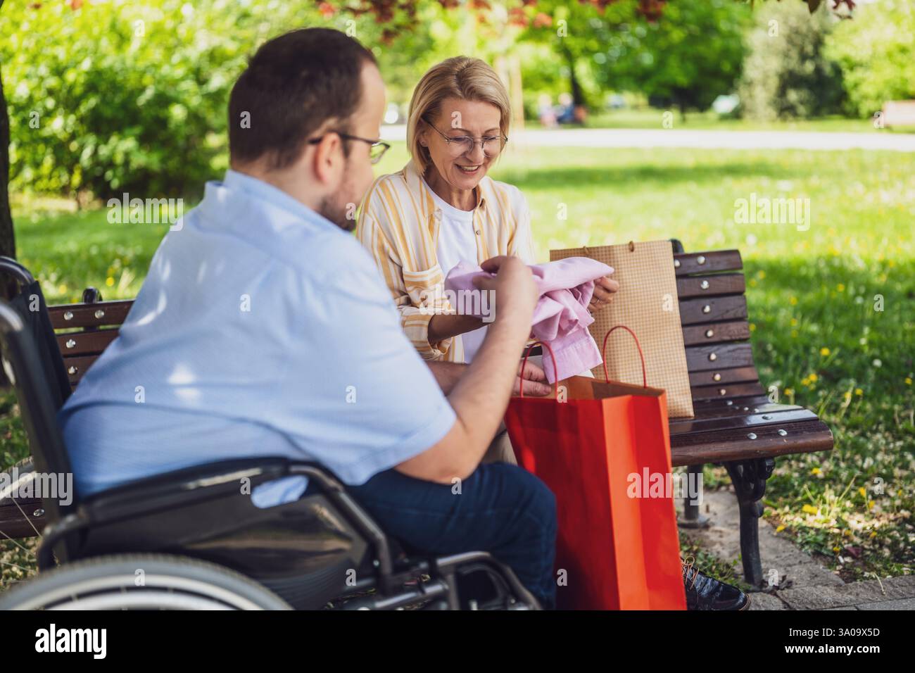 L'homme en fauteuil roulant passe du temps avec sa mère dans le parc. Ils parlent après avoir fait du shopping. Banque D'Images