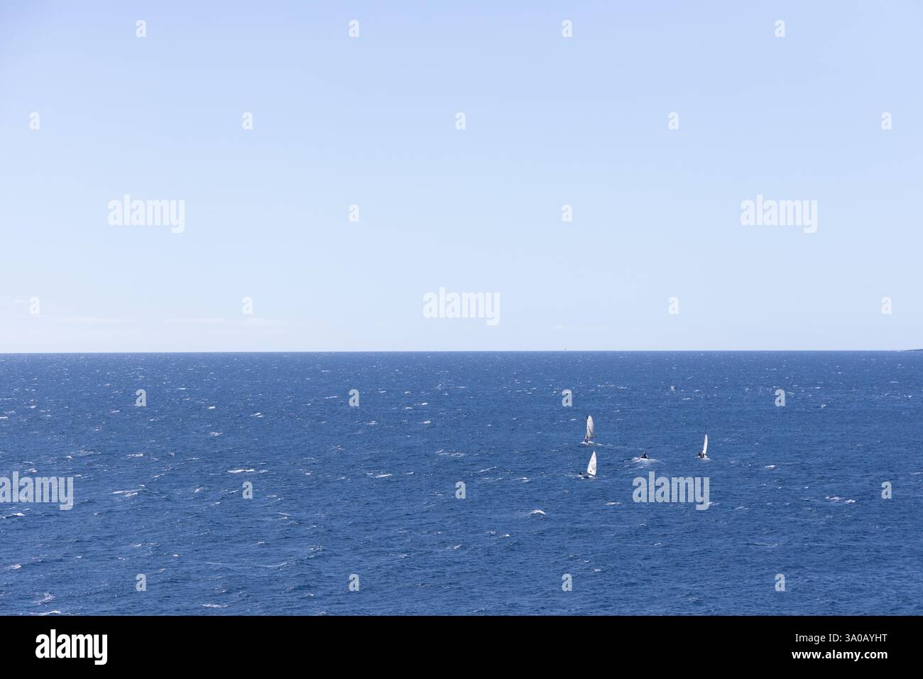 Une vaste étendue d'océan bleu profond avec de petits voiliers dispersés à l'horizon sous un ciel dégagé. Un paysage marin serein et minimaliste. Banque D'Images