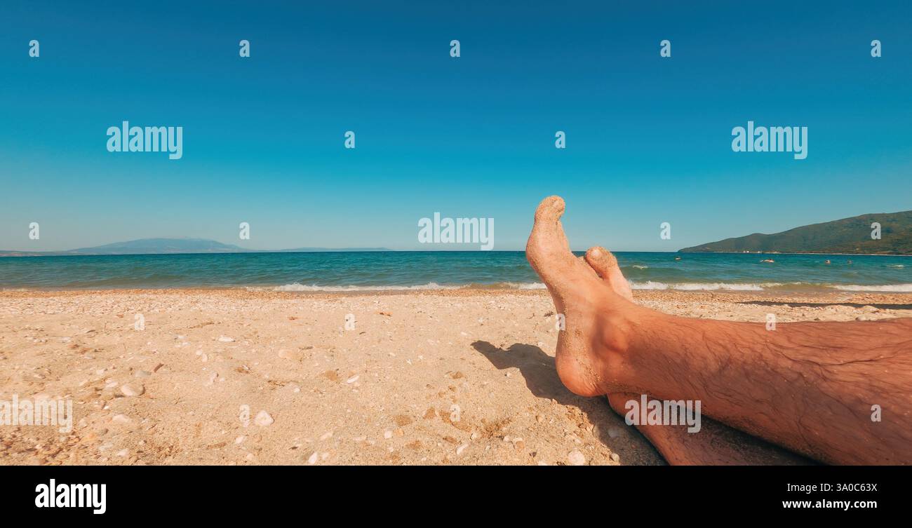 Détente sur la plage de sable, gros plan des pieds masculins, mise au point sélective Banque D'Images