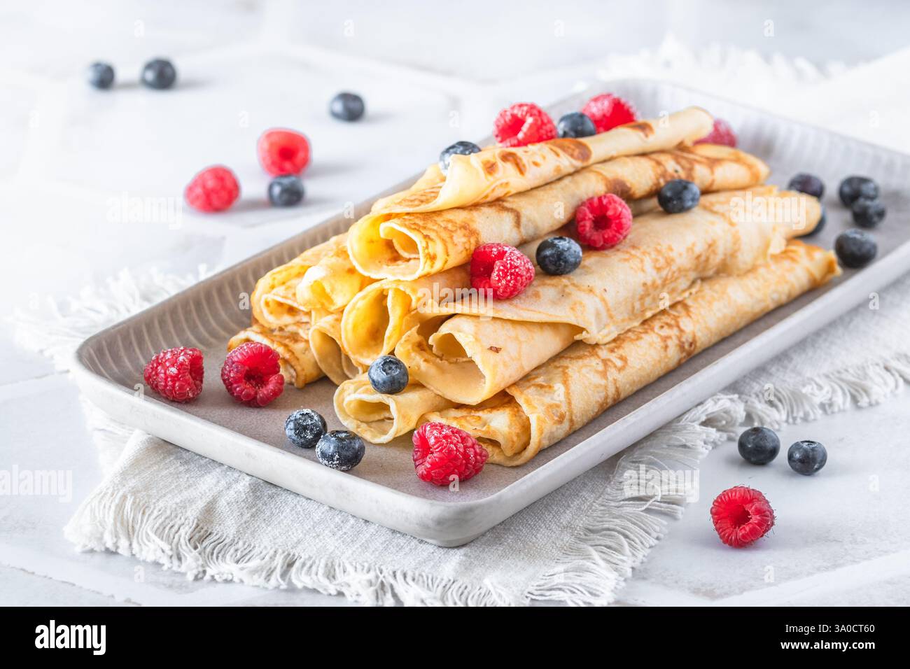 Assiette avec pile de crêpes roulées avec des rasperries et des bleuets sur fond blanc Banque D'Images