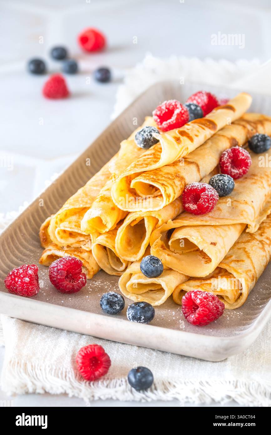 Assiette avec pile de crêpes roulées avec des rasperries et des bleuets sur fond blanc, vertical Banque D'Images