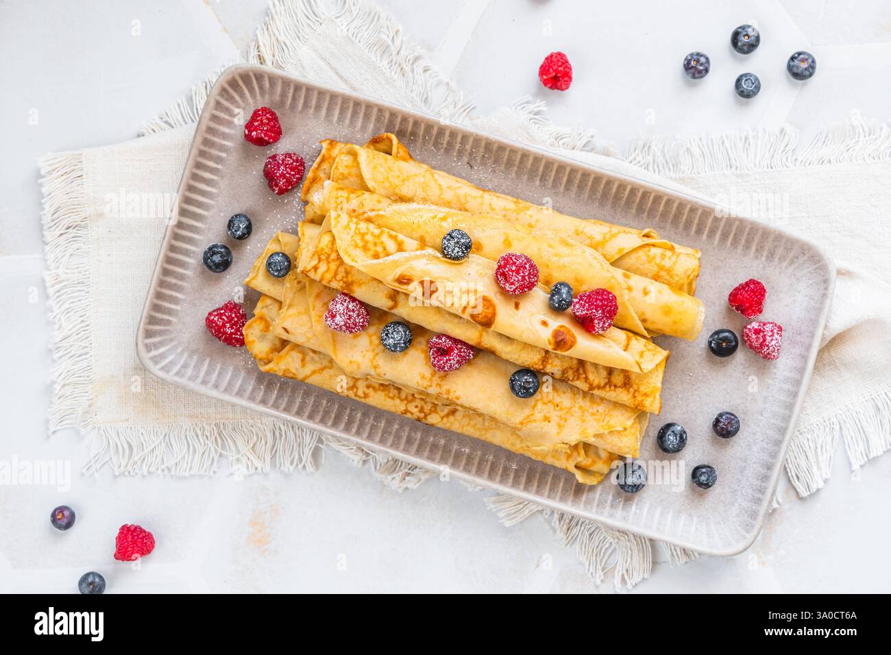 Assiette avec pile de crêpes roulées avec des rasperries et des bleuets sur fond blanc, vue de dessus Banque D'Images