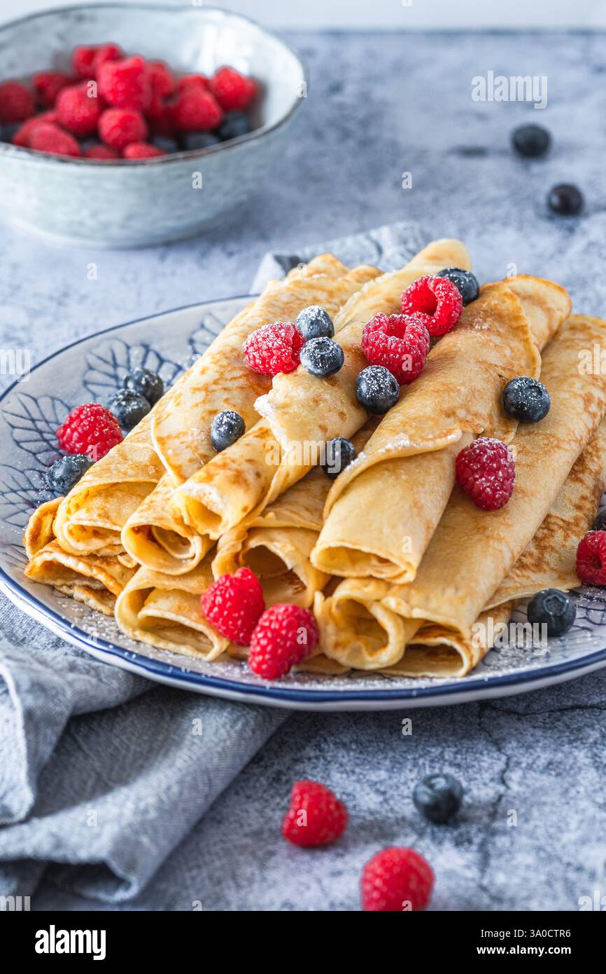 Assiette avec pile de crêpes roulées avec des rasperries et des bleuets sur fond bleu clair, verticale Banque D'Images