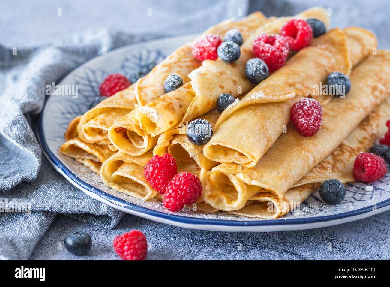 Assiette avec pile de crêpes roulées avec des rasperries et des bleuets sur fond bleu clair Banque D'Images