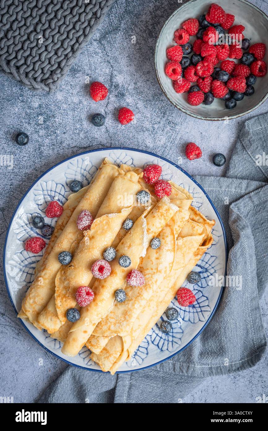 Assiette avec pile de crêpes roulées avec des rasperries et des bleuets sur fond bleu clair, vue de dessus Banque D'Images
