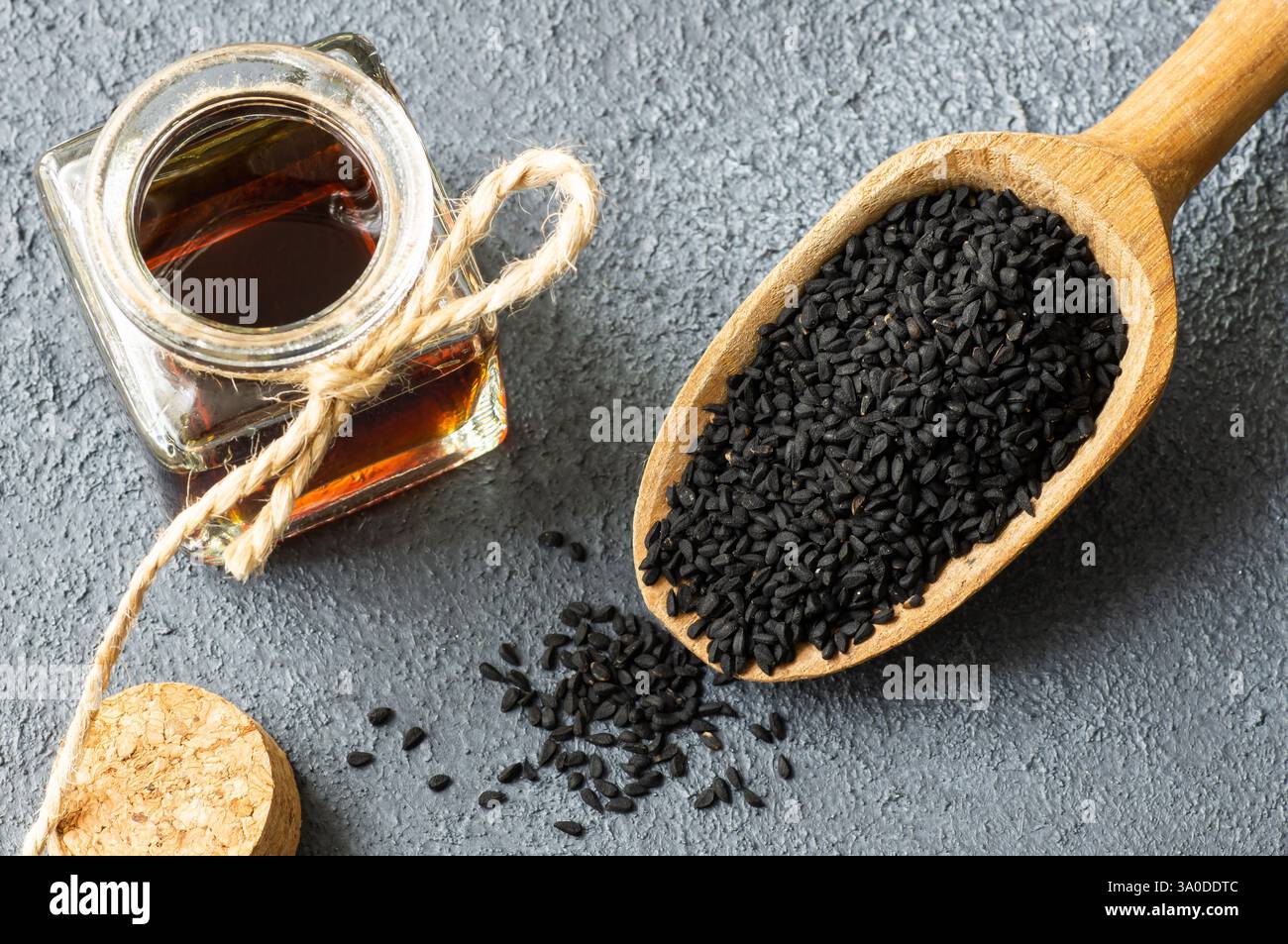 Bouteille en verre d'huile essentielle de graines de cumin noir, Nigella Sativa en cuillère sur fond rustique. Phytothérapie organique pour de nombreuses maladies, cumin noir Banque D'Images