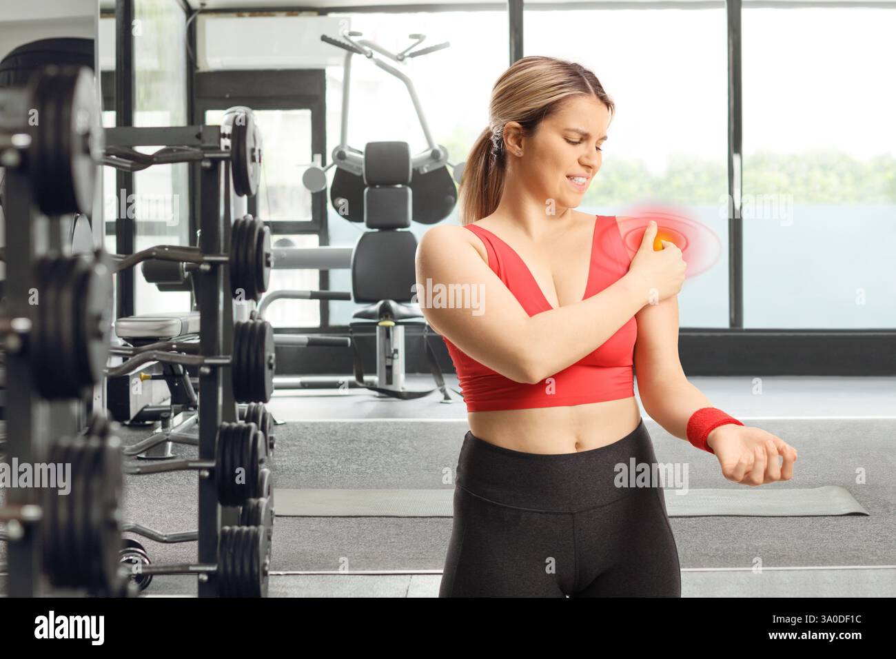 Jeune femme avec douleur dans l'exercice d'épaule avec un haltère dans un gymnase Banque D'Images