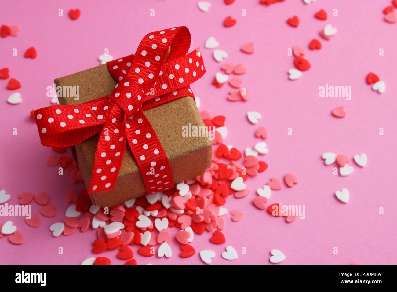 Boîte cadeau avec noeud en ruban rouge avec des points blancs entourés de coeurs colorés Banque D'Images