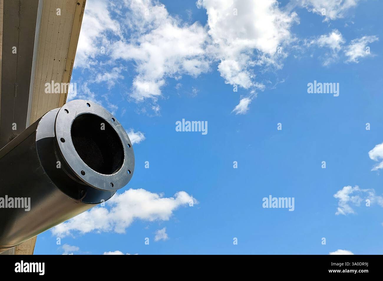 Haut au-dessus, un solide tuyau d'échappement du générateur s'étend vers le ciel bleu expansif, encadré par des nuages blancs doux dérivant paisiblement. Banque D'Images