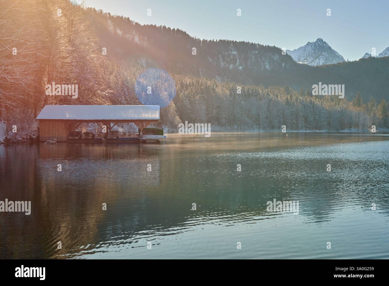 Cette photographie haute résolution capture un lever de soleil d'hiver à couper le souffle sur un lac serein. Le point focal est un hangar à bateaux en bois rustique, partiellement s. Banque D'Images