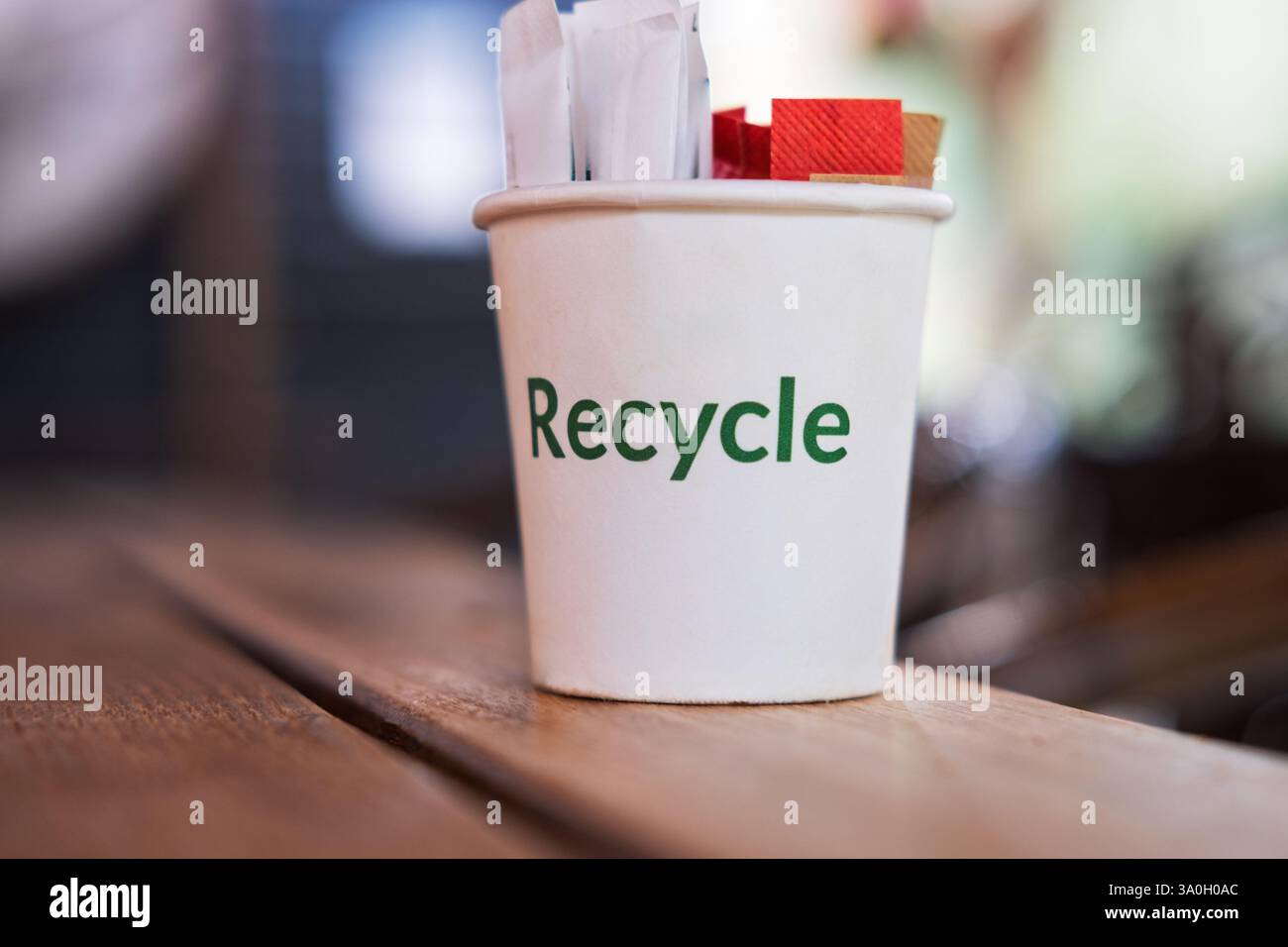 Un gros plan montre un gobelet en papier blanc avec le mot « recycler » imprimé en vert sur le côté, assis sur une table en bois. Banque D'Images