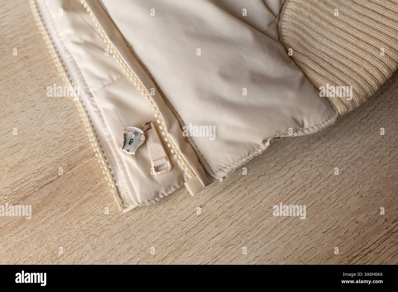 Gros plan d'une fermeture éclair cassée sur une veste beige clair. Détails du coureur endommagé, la texture du tissu et l'élastique tricoté. Banque D'Images