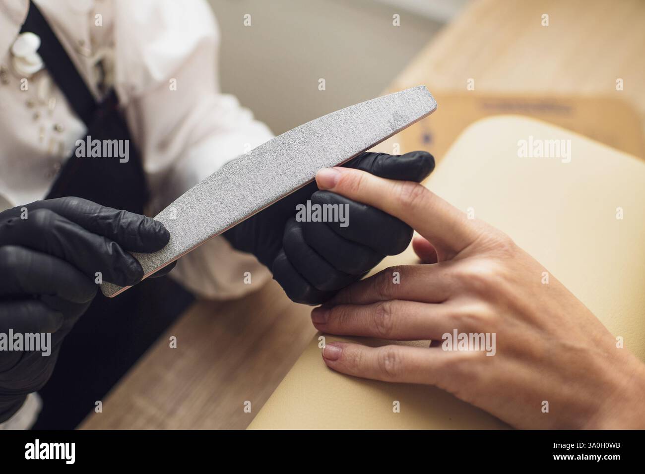 Une manucure en gants noirs lime soigneusement les ongles du client avec une lime dans un salon de beauté. Soin professionnel des mains Banque D'Images