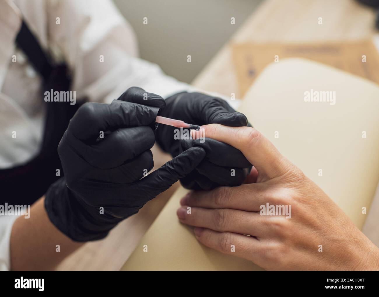 Une manucure en gants et un masque de protection applique soigneusement le vernis sur les ongles du client dans un salon de beauté. Gros plan Banque D'Images