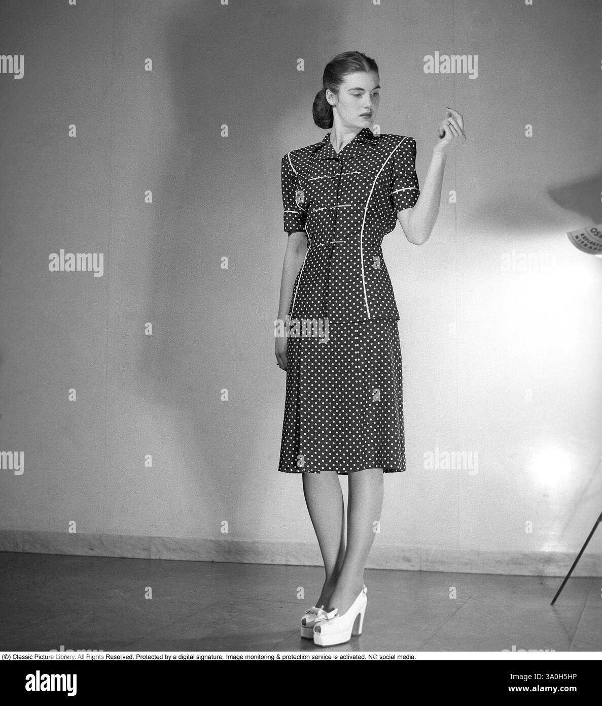 Fashion 1946, une jeune mannequin habillée à la mode de l'après-guerre. La robe avec des manches courtes atteignant en dessous des genoux est en tissu sombre avec un motif de points blancs. Kristoffersson réf Y86-6 Banque D'Images