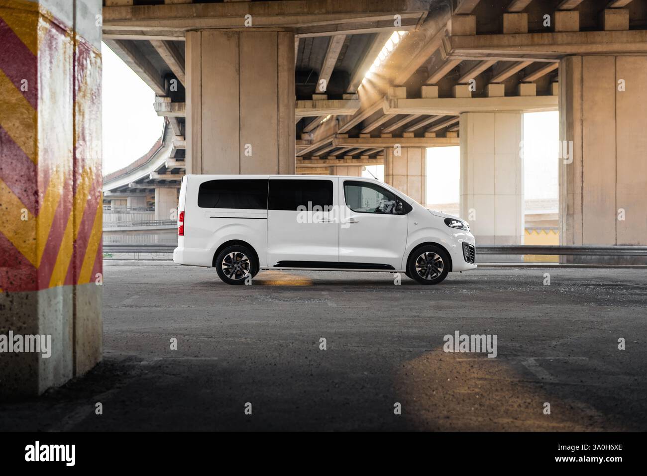 Vue latérale de l'Opel Vivaro blanc. Vue en perspective décroissante de la fourgonnette sous deux ponts autoroutiers en béton en arrière-plan au coucher du soleil. Banque D'Images