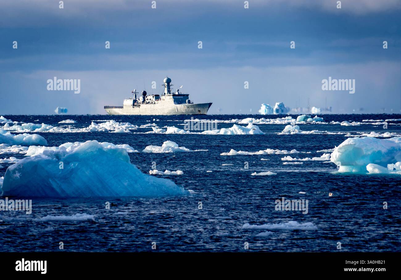 Un navire de recherche navigue dans des eaux glacées, entouré d'icebergs flottants. Le navire est équipé pour l'exploration arctique, avec un ciel nuageux dans le Banque D'Images