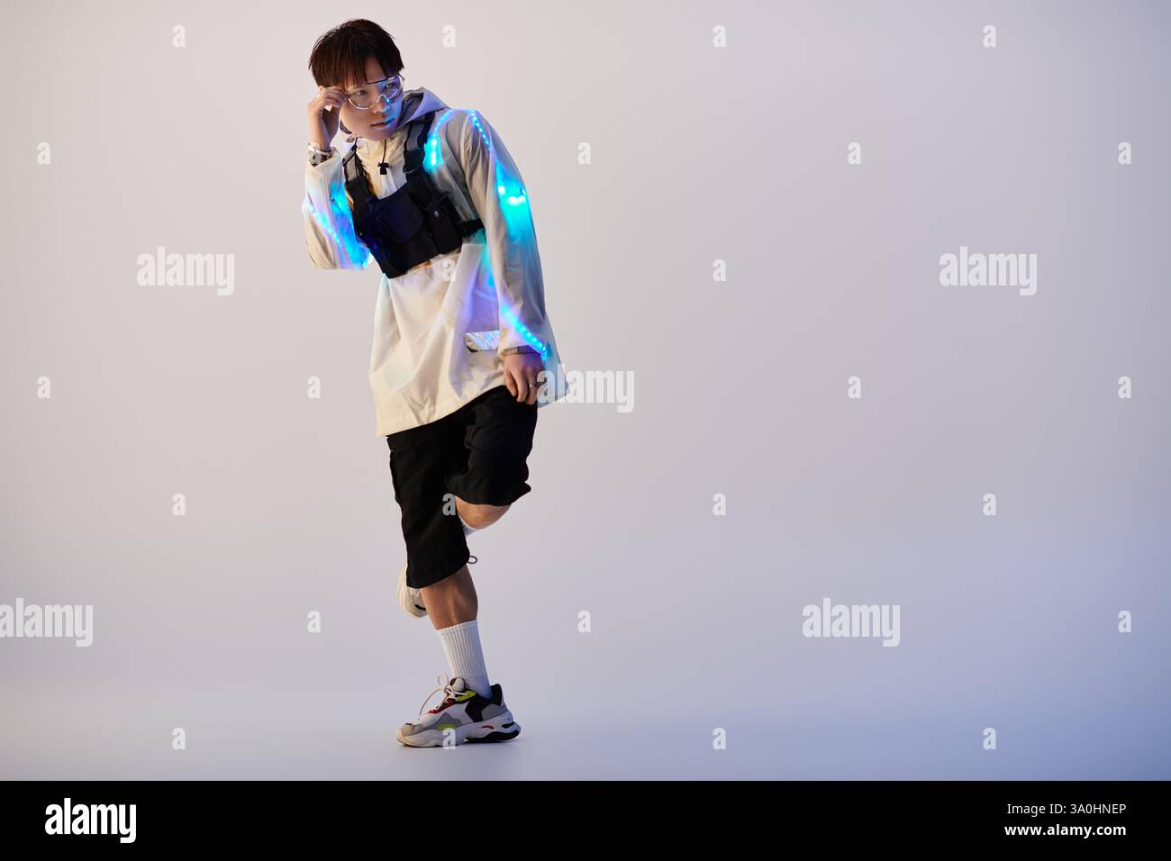 Un jeune homme asiatique élégant pose en toute confiance avec des éléments lumineux, incarnant la culture urbaine. Banque D'Images