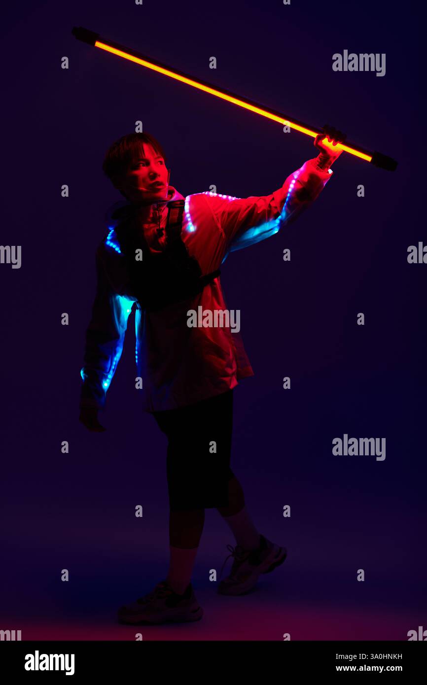 Un jeune homme asiatique élégant brandit un bâton lumineux au milieu des lumières vibrantes. Banque D'Images