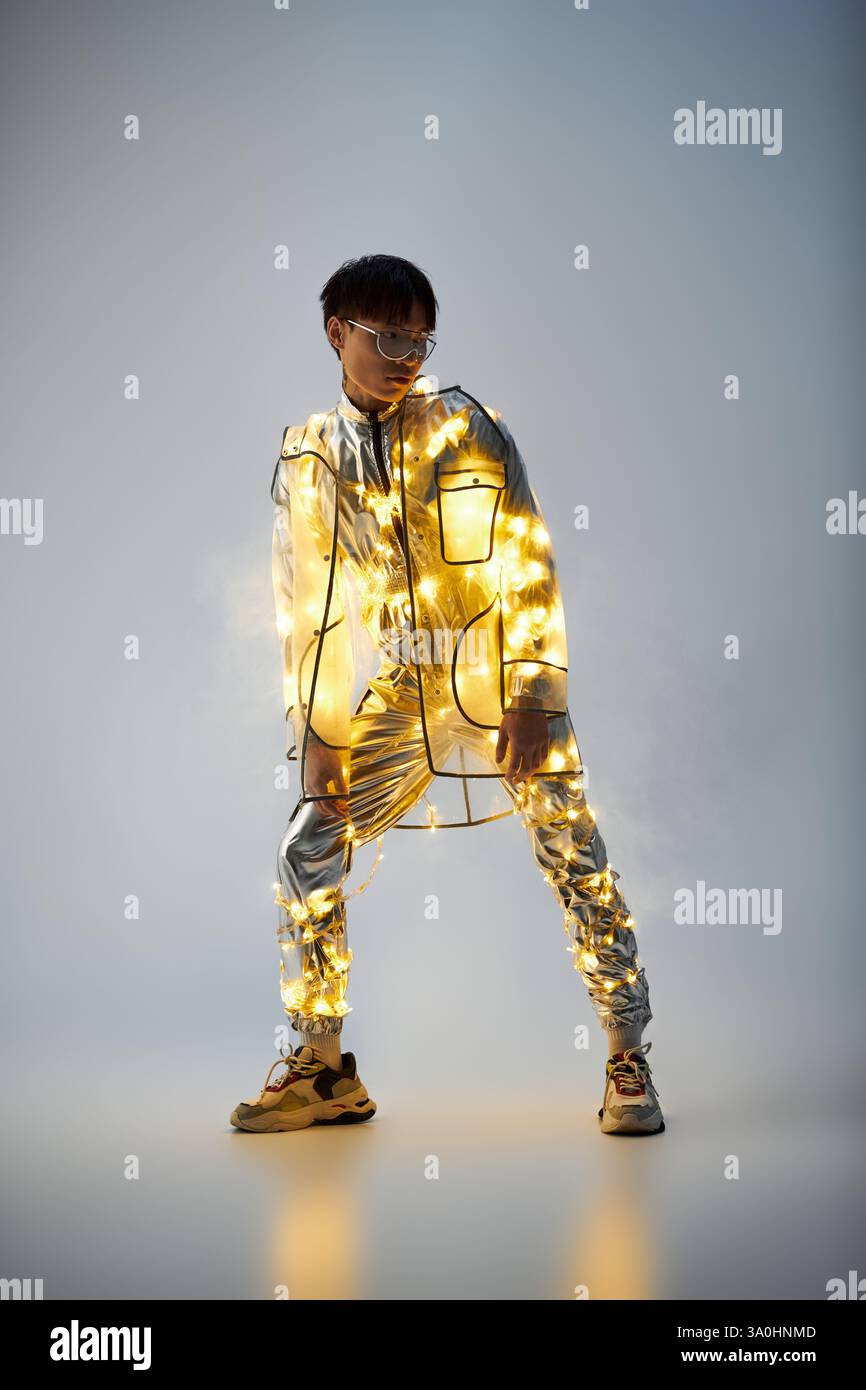 Jeune homme se tient confiant dans une tenue chatoyante ornée de lumières, embrassant un style créatif. Banque D'Images