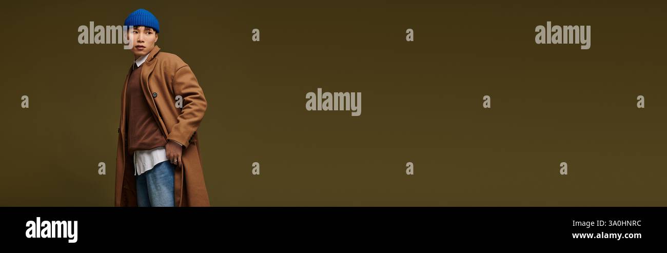 Un jeune et beau homme asiatique vêtu d'un manteau tendance et d'un bonnet bleu respire le style et la confiance. Banque D'Images