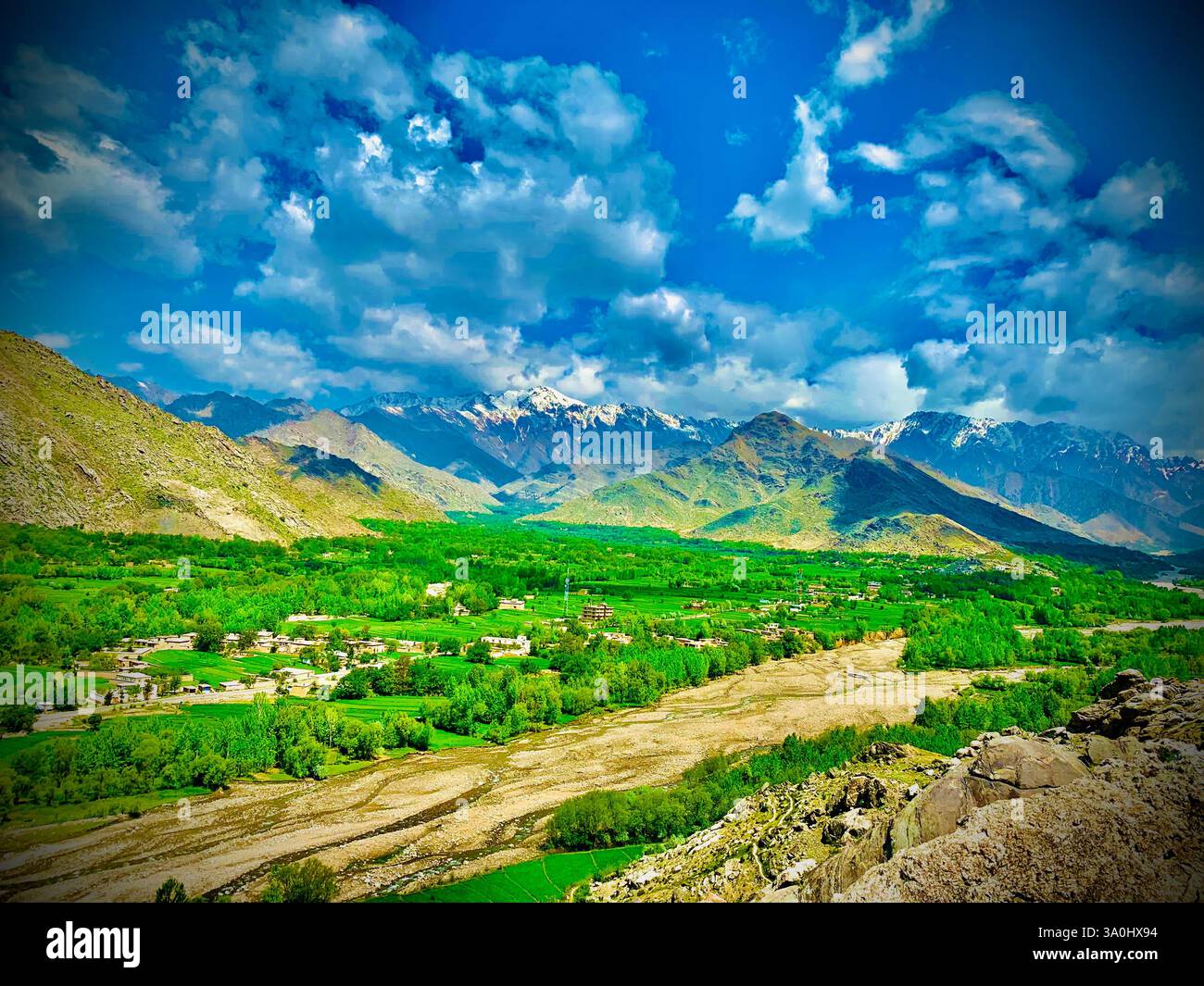 Terres agricoles verdoyantes avec des montagnes imposantes en arrière-plan et un sentier enneigé, Afghanistan. - Image de stock capturée avec un smartphone