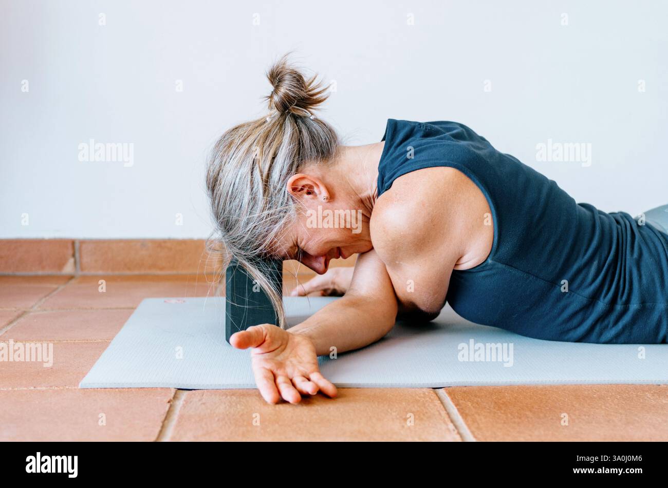 Femme pratiquant le yin yoga étirement du bras croisé, tête soutenue par le bloc Banque D'Images