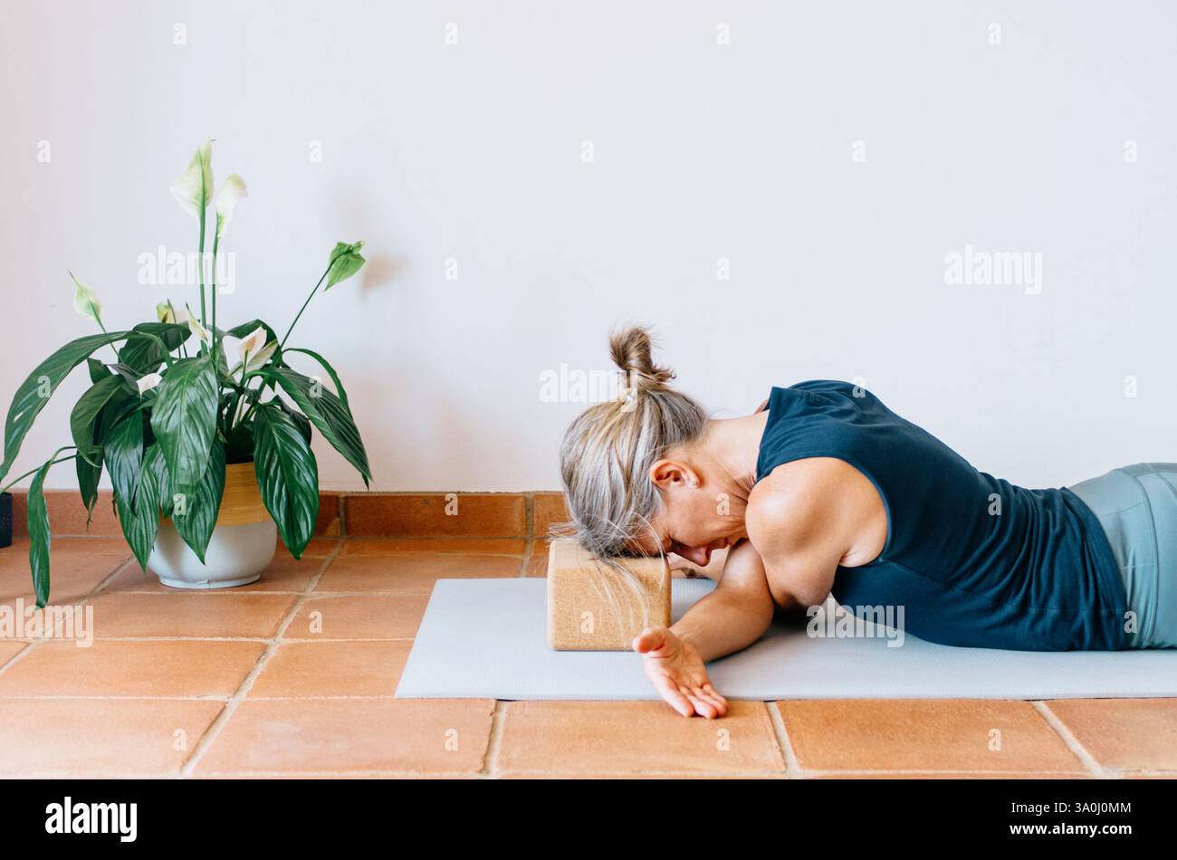 Femme pratiquant le yin yoga étirement du bras croisé, tête soutenue par un bloc de liège Banque D'Images