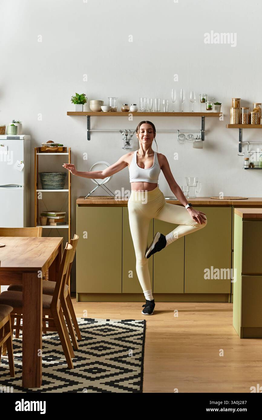 Une jeune femme danse gracieusement dans une cuisine lumineuse tout en portant des leggings et un soutien-gorge de sport. Banque D'Images