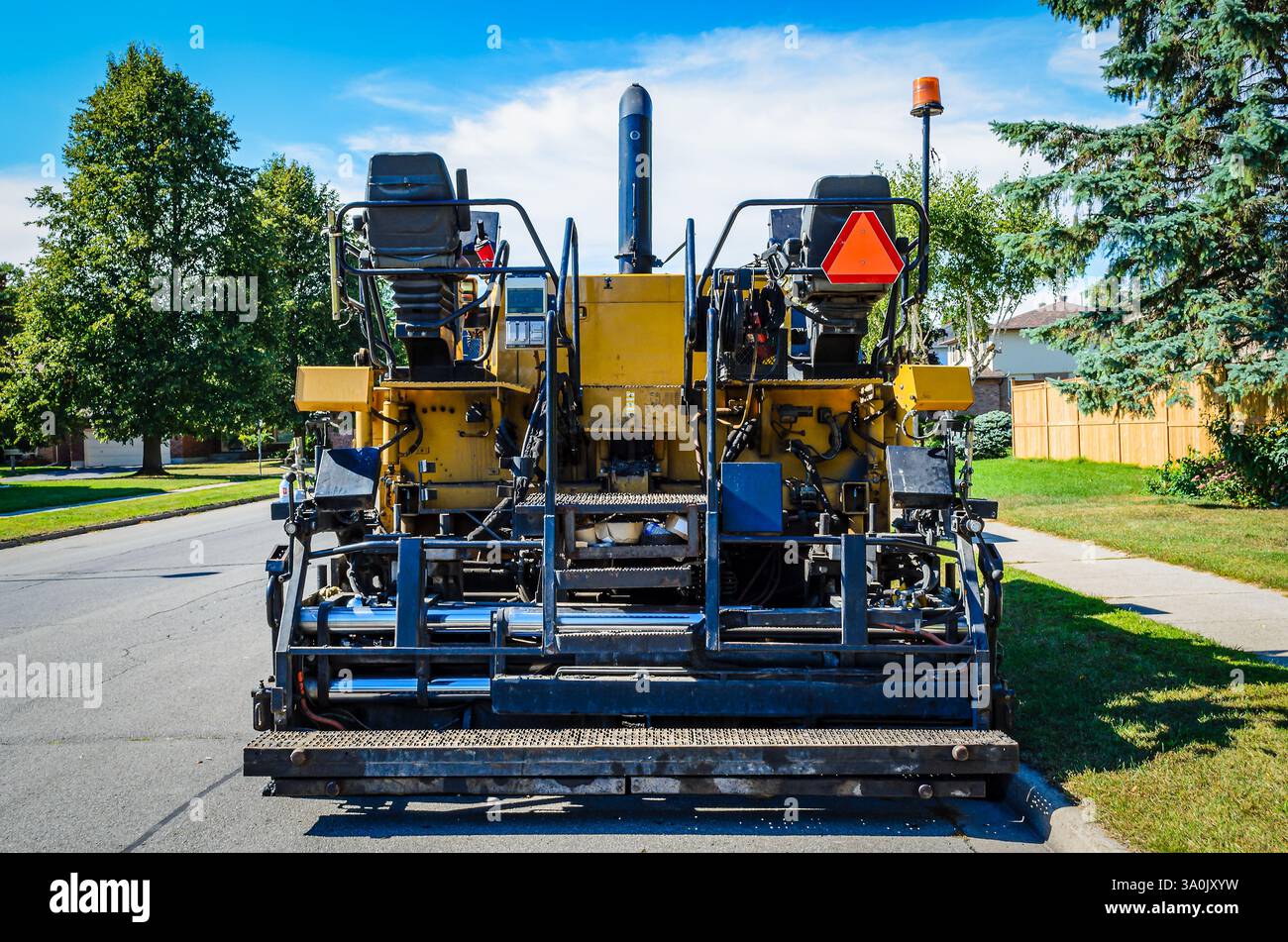Vue arrière d'un paveur routier stationné sur une rue résidentielle sous un ciel bleu. Banque D'Images