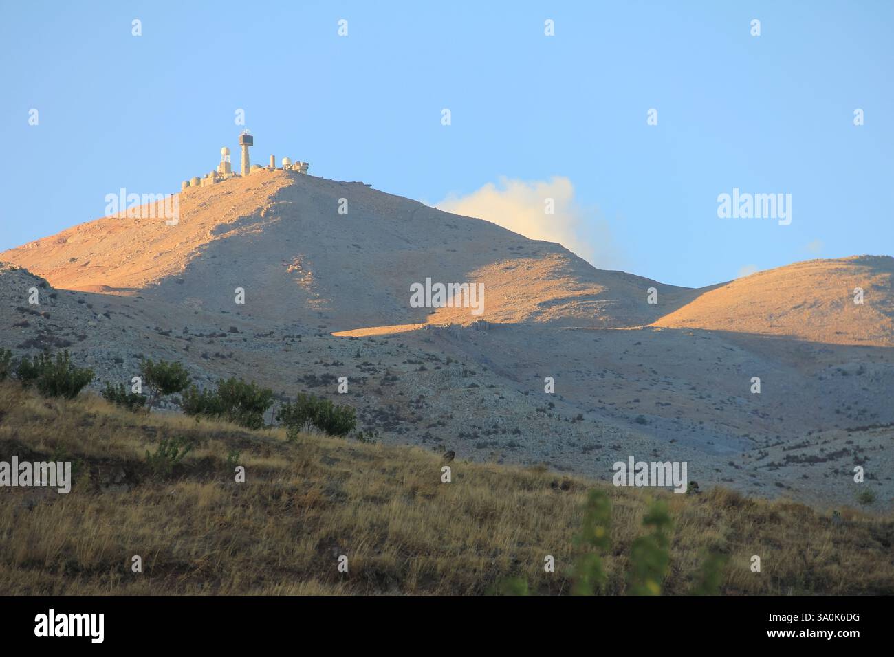 Une vue panoramique d'une montagne de radars militaires entourés d'herbe sèche et d'arbres clairsemés à la lumière du soleil. Le ciel bleu met en valeur la sérénité et l'être naturel Banque D'Images