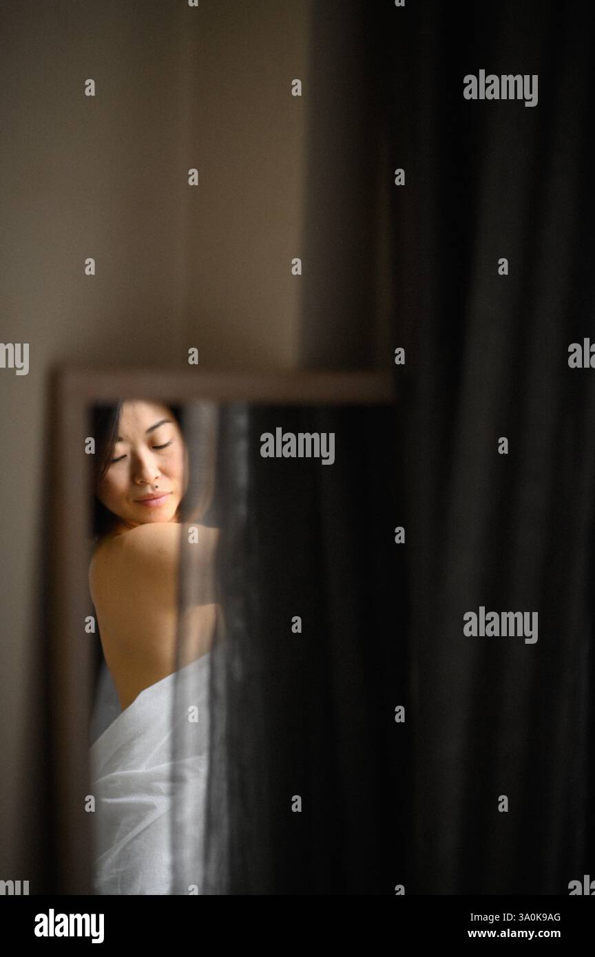 Le miroir reflète le visage d’une jeune femme, son expression douce et contemplative alors qu’elle regarde sa propre image. Banque D'Images