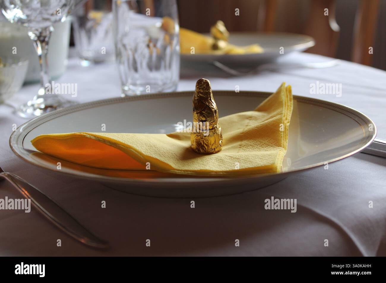 Cadre de table de Pâques élégant avec lapin au chocolat doré sur serviette jaune - repas de vacances festif, fête du printemps, décoration raffinée et atmosphère chaleureuse Banque D'Images