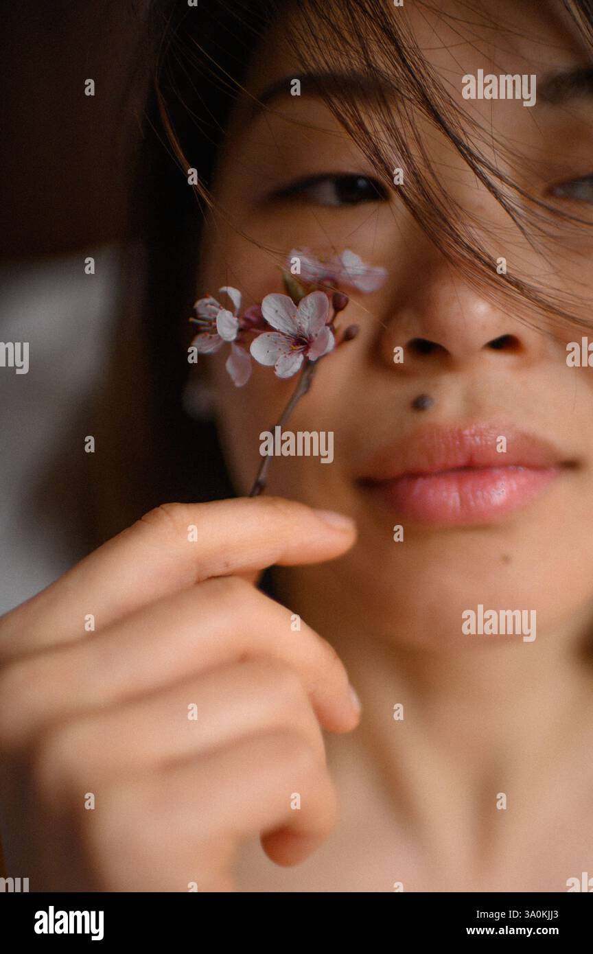 Femme tenant une fleur rose près de son visage – Un moment gracieux où une femme tient doucement une fleur rose près de son visage, exsudant douceur et élégance. Banque D'Images