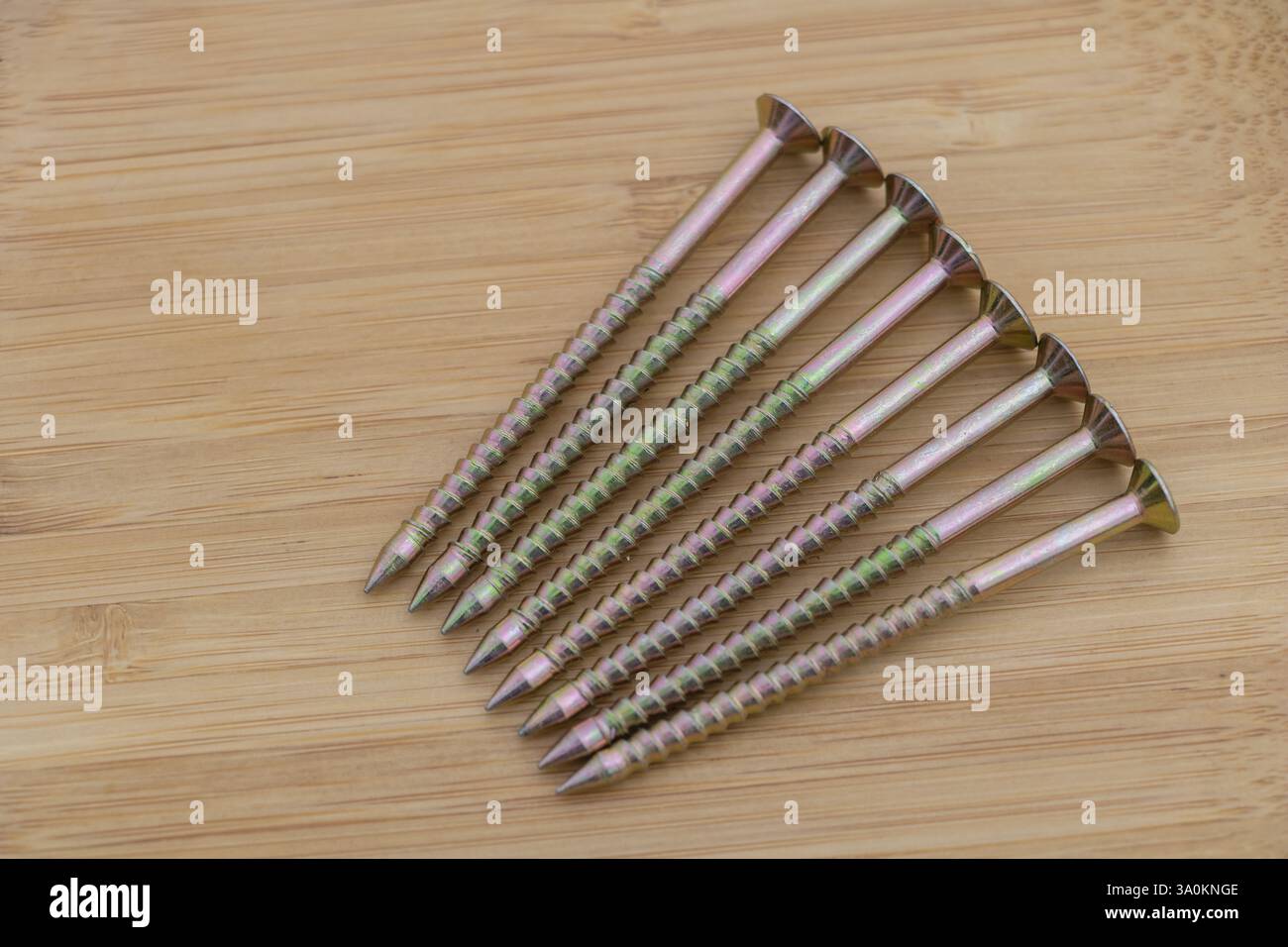 6 clous de menuisier à tête Phillips-point reposant sur une surface en bois clair, avec des têtes de clous de couleur jaune-vert. Banque D'Images