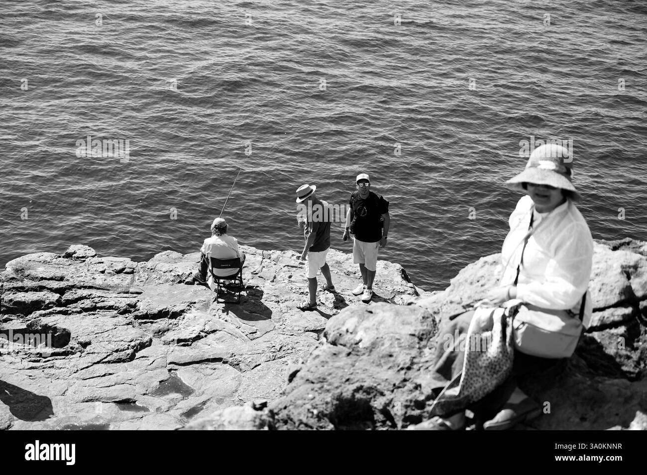 Journée tranquille au bord de la mer, avec pêche et détente sur les falaises rocheuses, en monochrome Banque D'Images