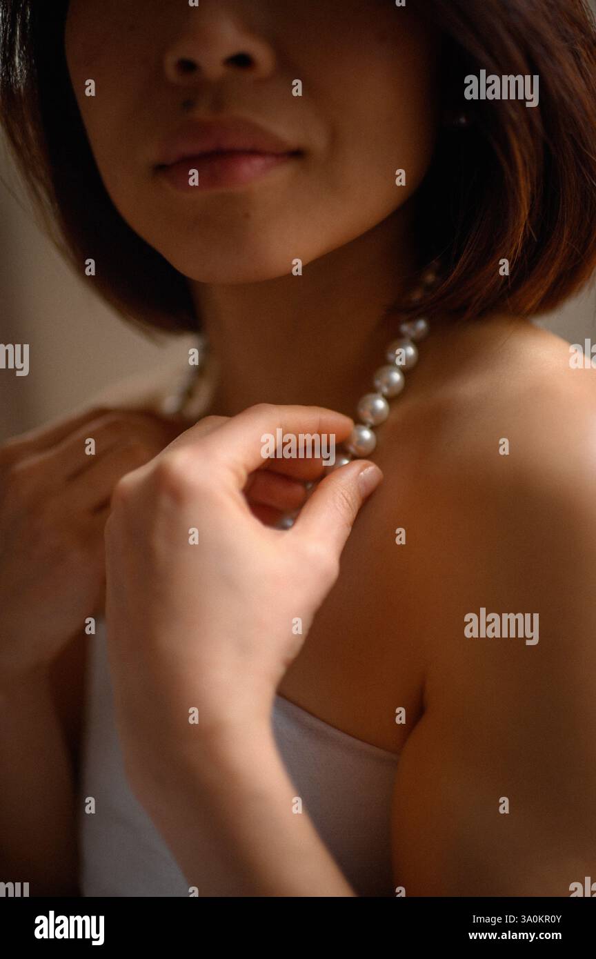Une jeune femme regarde doucement, portant une élégante boucle d'oreille en perles et un collier assorti. Banque D'Images
