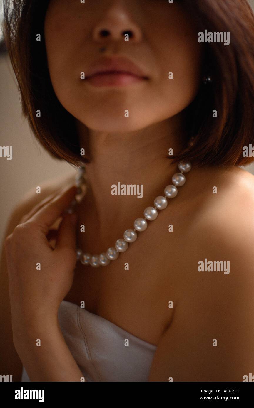 Une jeune femme regarde doucement, portant une élégante boucle d'oreille en perles et un collier assorti. Banque D'Images
