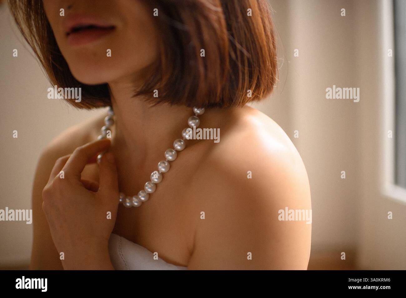 Une jeune femme regarde doucement, portant une élégante boucle d'oreille en perles et un collier assorti. Banque D'Images