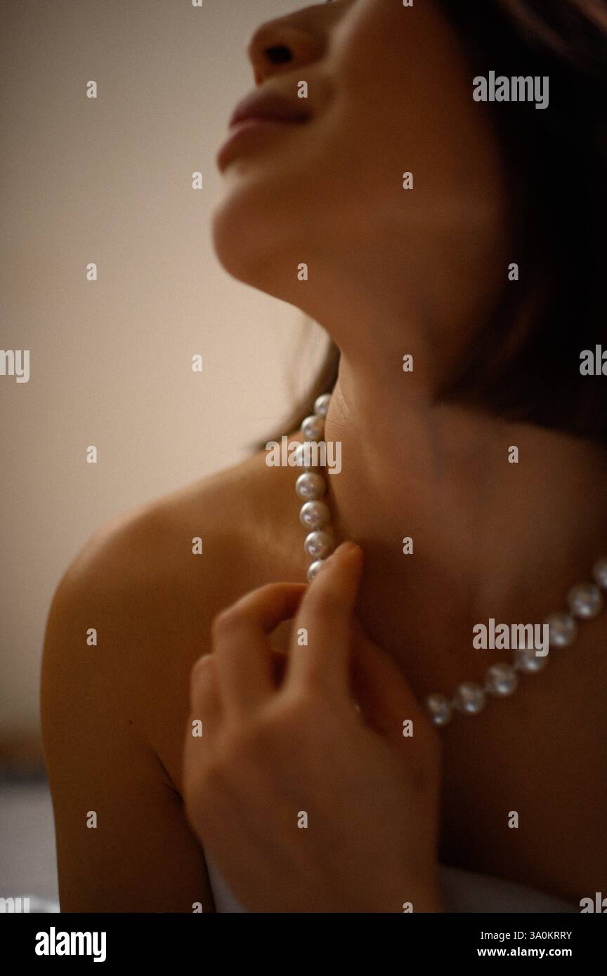 Une jeune femme regarde doucement, portant une élégante boucle d'oreille en perles et un collier assorti. Banque D'Images