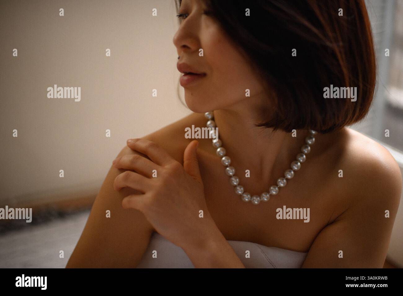 Une jeune femme regarde doucement, portant une élégante boucle d'oreille en perles et un collier assorti. Banque D'Images