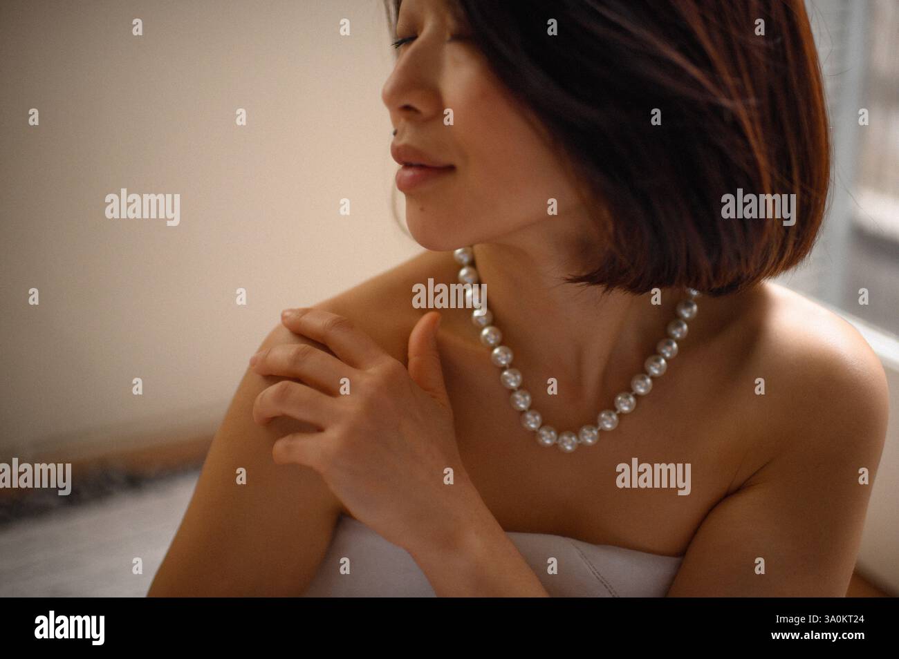 Une jeune femme regarde doucement, portant une élégante boucle d'oreille en perles et un collier assorti. Banque D'Images