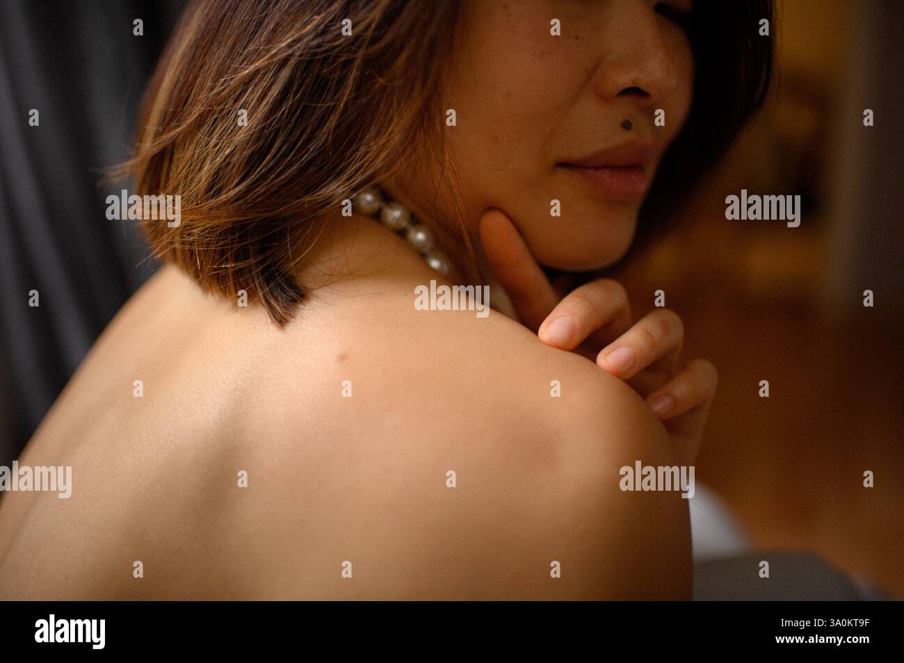 Une jeune femme regarde doucement, portant une élégante boucle d'oreille en perles et un collier assorti. Banque D'Images