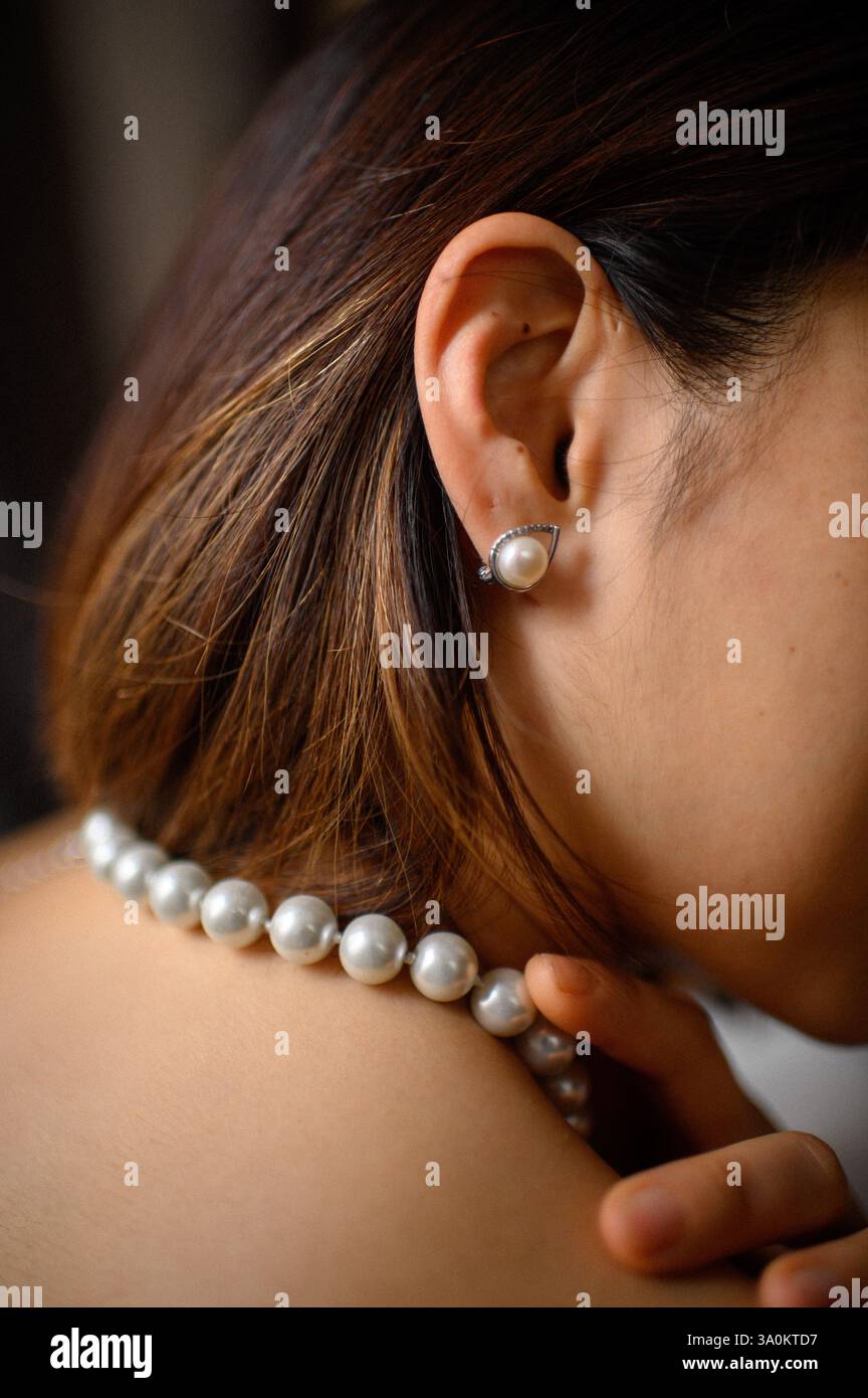 Une jeune femme regarde doucement, portant une élégante boucle d'oreille en perles et un collier assorti. Banque D'Images