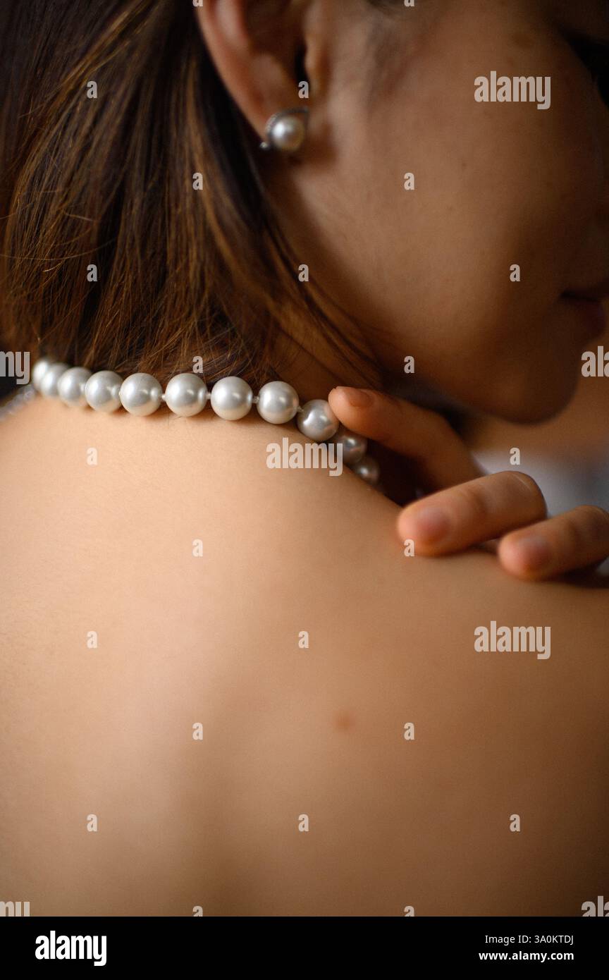 Une jeune femme regarde doucement, portant une élégante boucle d'oreille en perles et un collier assorti. Banque D'Images