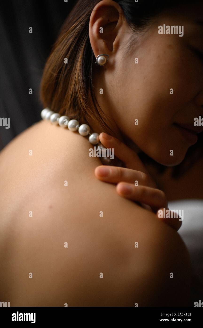 Une jeune femme regarde doucement, portant une élégante boucle d'oreille en perles et un collier assorti. Banque D'Images